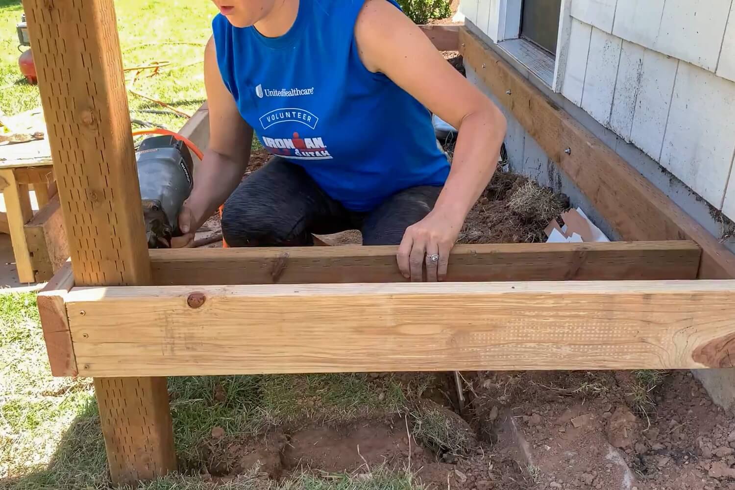 Crystel kneeling inside the porch frame to install a deck joist.