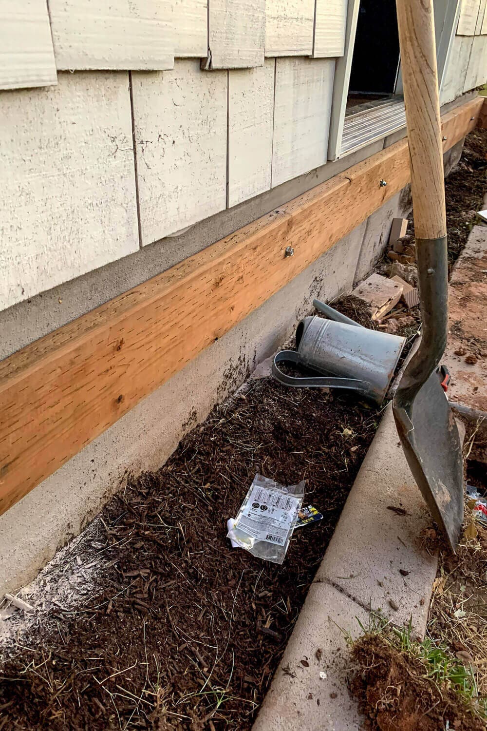 Pressure-treated 2x6 ledger board attached to the concrete foundation of the house, with a shovel and hardware nearby.