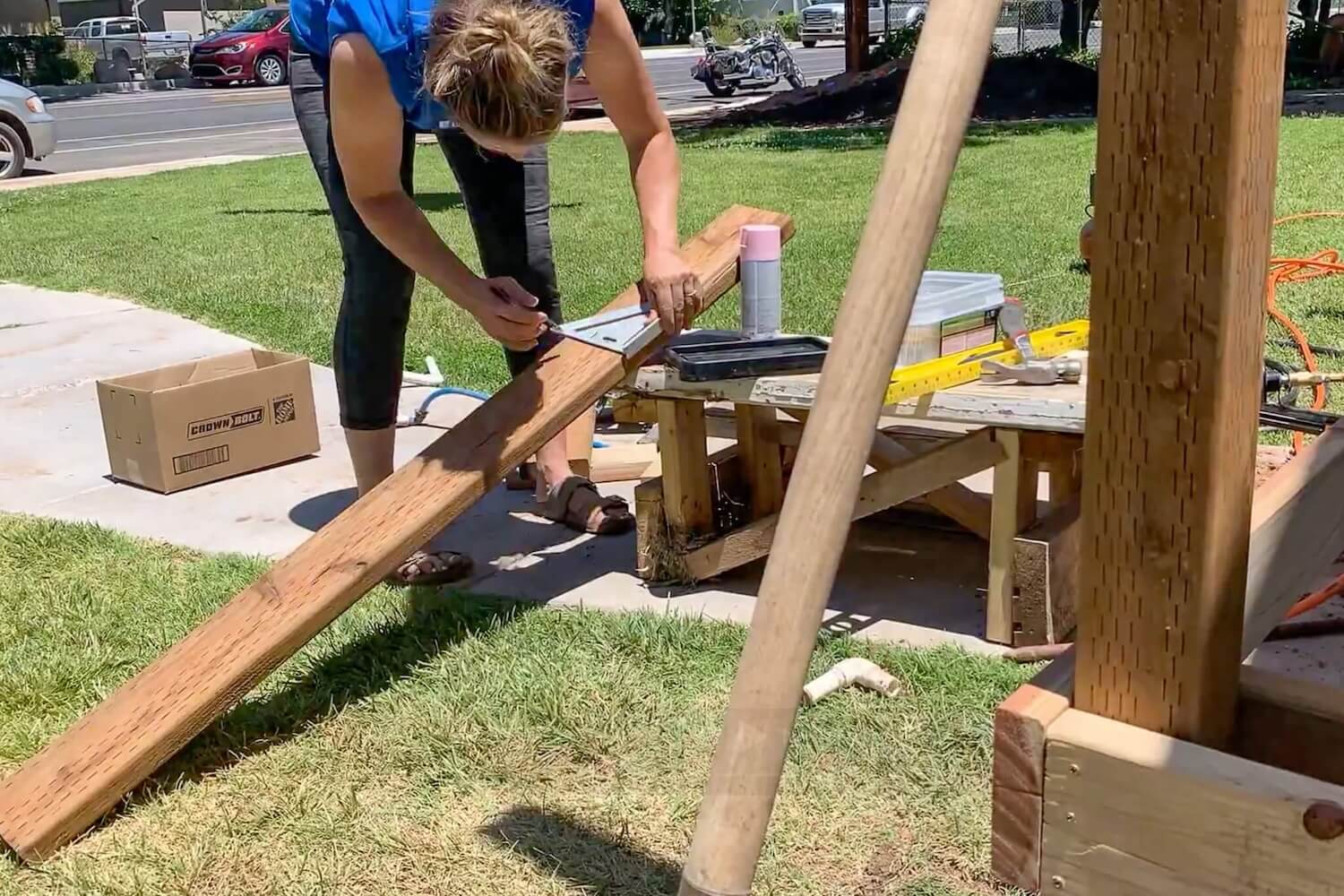 Crystel measuring and cutting a 2x6 deck joist on a sawhorse.