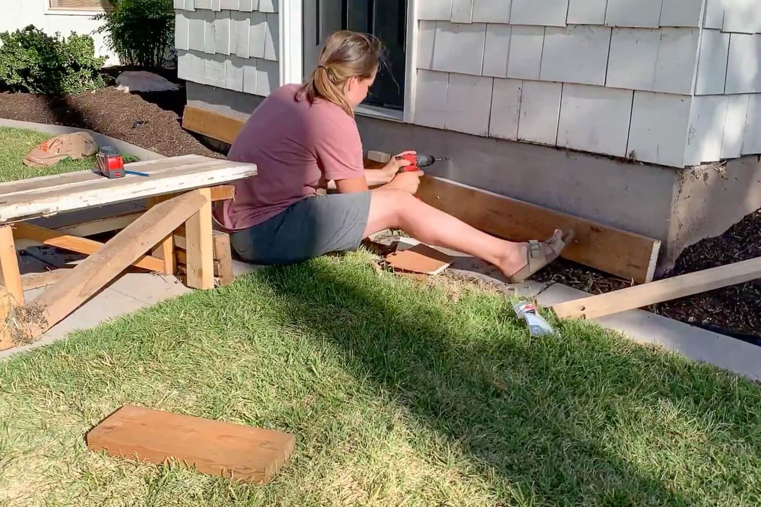 Crystel sitting on the grass, aligning and leveling the ledger board against the house foundation.
