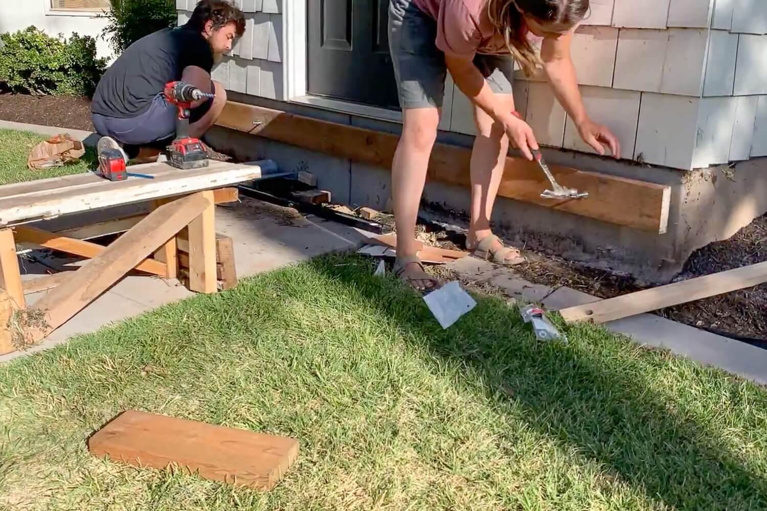 A helper drilling the ledger board while Crystel sets the masonry anchors into the concrete.