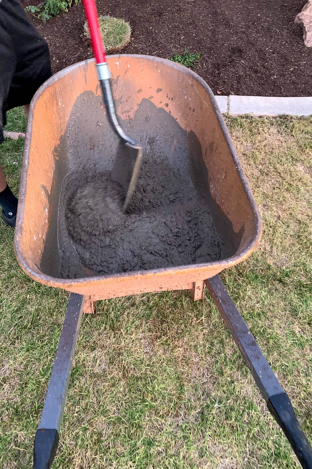 A wheelbarrow of mixed Quikrete concrete with a shovel, ready to pour around the porch posts.
