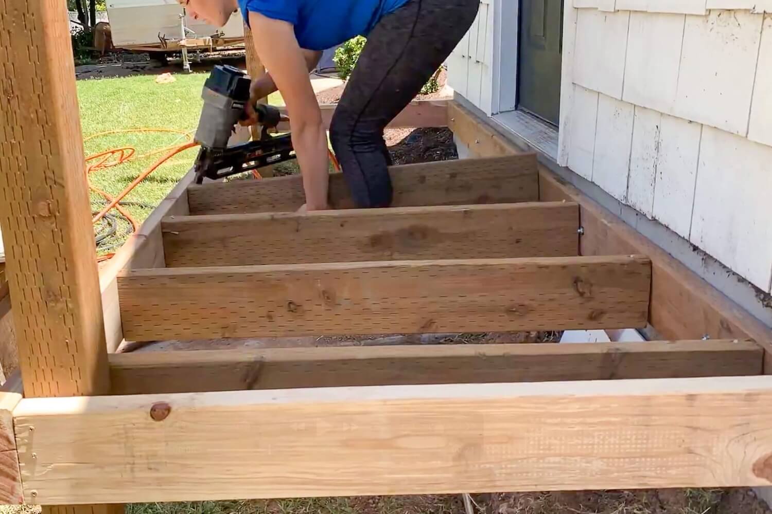 Crystel using a nail gun to toe-nail the deck joists into the rim board.