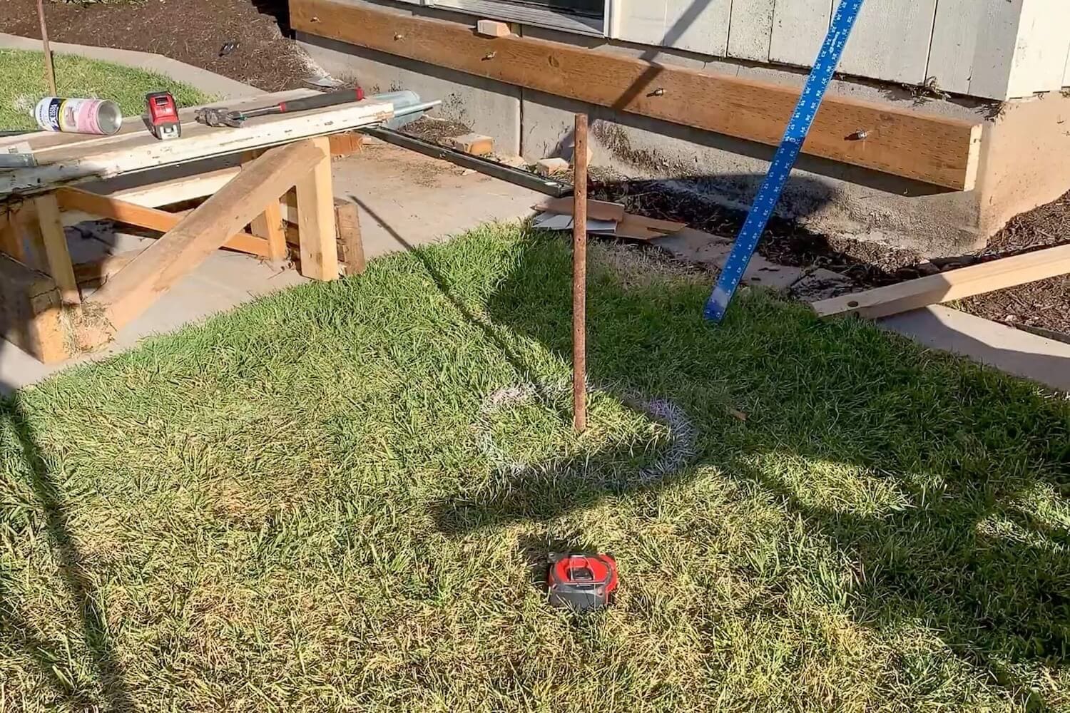 Post hole location marked with a stake, string line, and a spray-painted 12-inch circle on the grass.