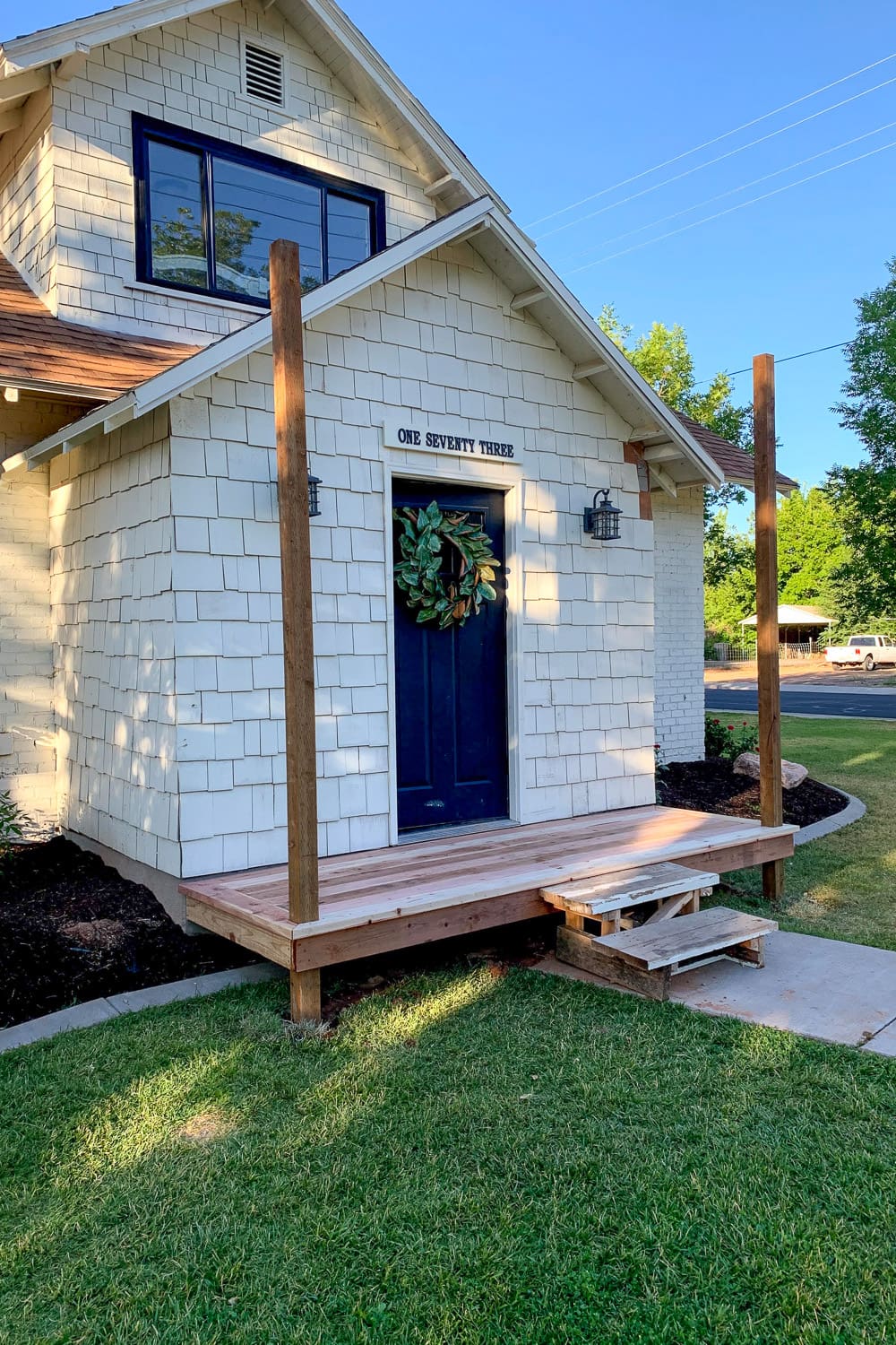 Completed DIY front porch deck and trim with bare posts and temporary pallet steps before the roof.