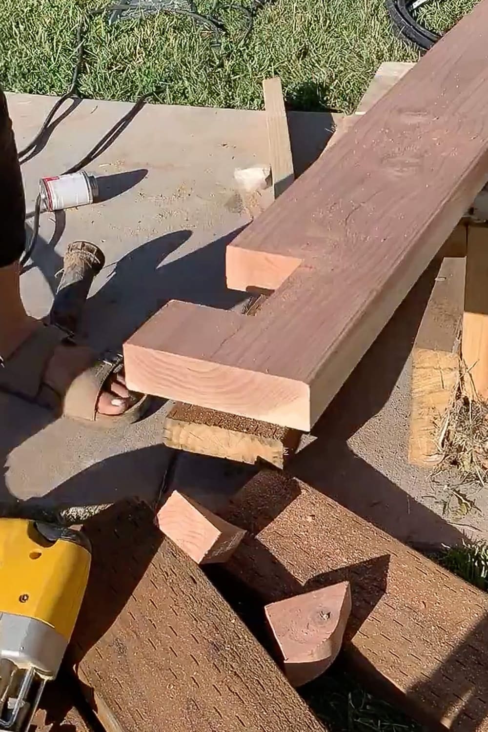 Two redwood porch trim boards with square notches cut out of the ends, with a jigsaw nearby.