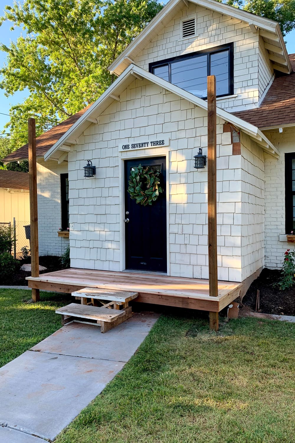 DIY front porch with newly installed wood deck boards and bare support posts, before the roof, with temporary pallet steps.