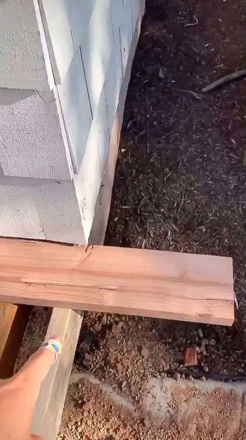 Redwood border trim board held against the house siding to mark the back board for a DIY front porch.