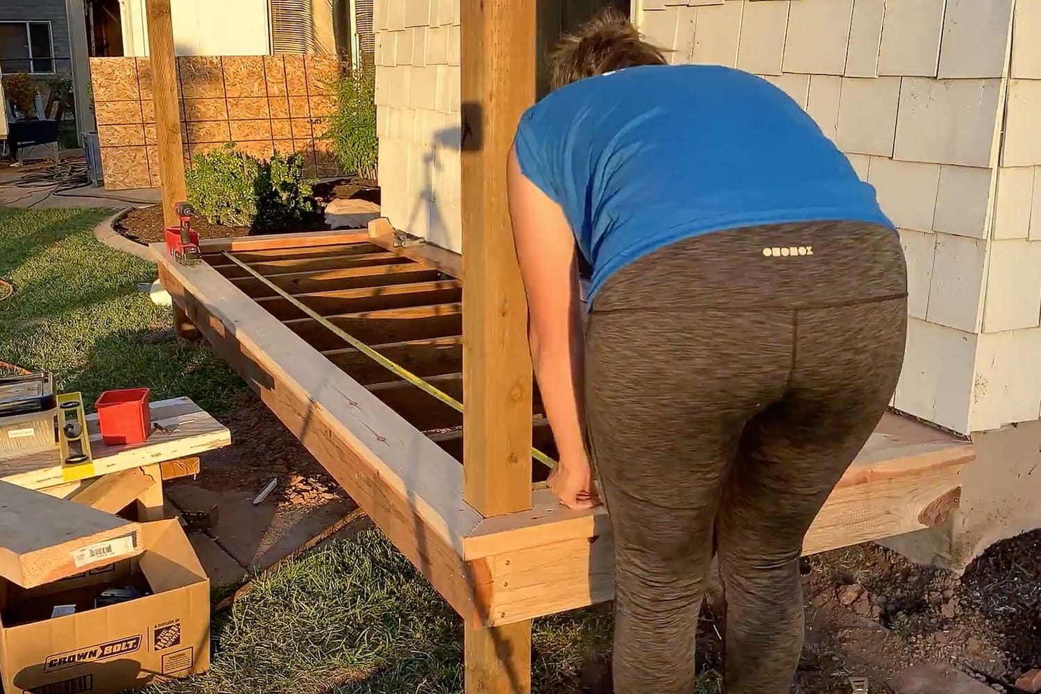 Woman measuring across the porch joists with a tape measure before laying the deck boards.