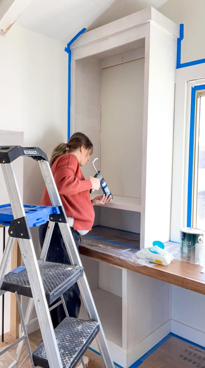 Woman caulking a built in cabinet