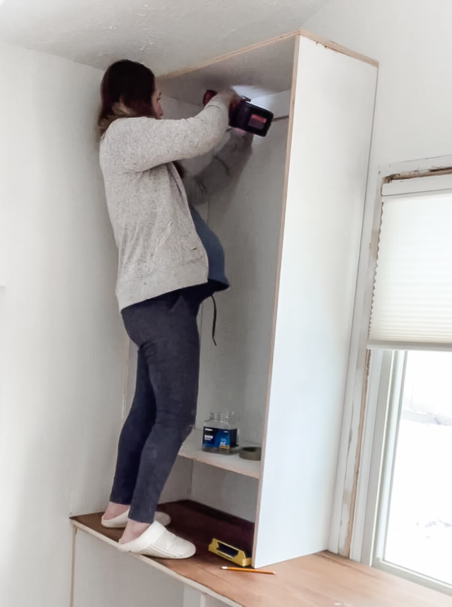 Woman screwing built in cabinet into the wall