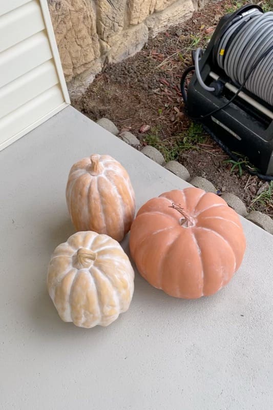 Faux terracotta pumpkins drying on a front porch after being painted with a textured baking soda mix.