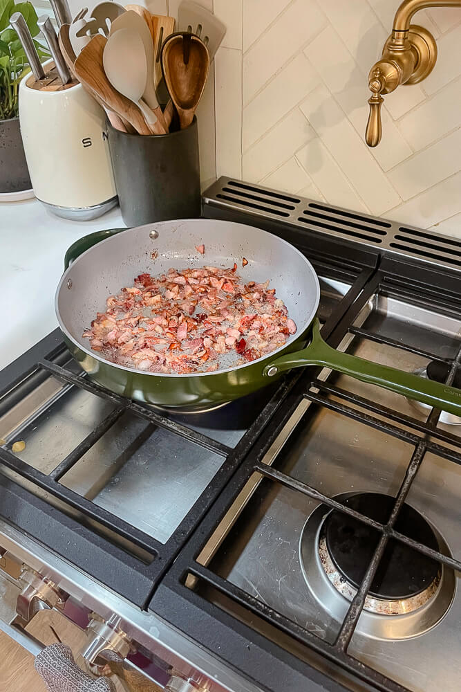 Bacon sizzling in a green skillet on a gas stovetop