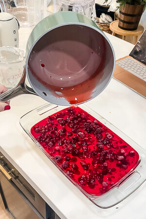 Raspberry gelatin being poured over the raspberry layer in the glass dish, completing the raspberry pretzel pie.