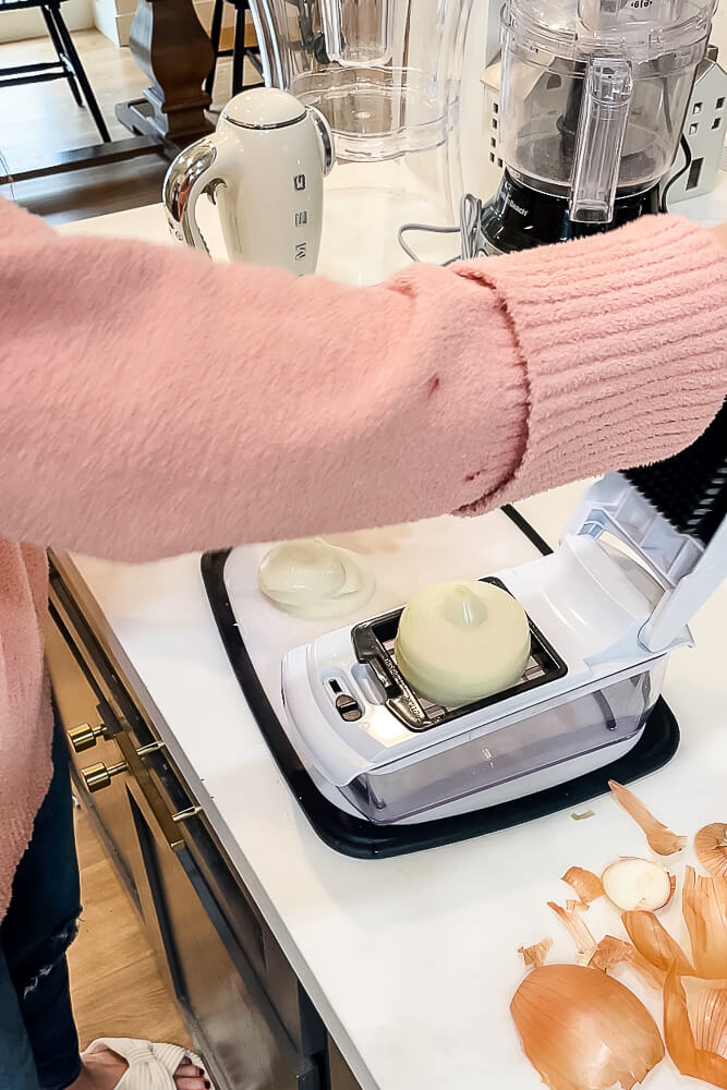 Close-up of onions being chopped with a manual food chopper on a white countertop, part of the Thanksgiving stuffing preparation.