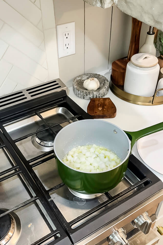 Chopped onions and celery being sautéed in a green pot on the stove for Thanksgiving stuffing.