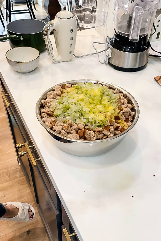 A large mixing bowl filled with bread cubes, sautéed onions, and celery, ready to be mixed into Thanksgiving stuffing.