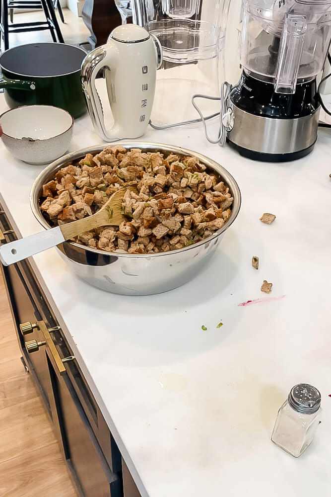 A bowl of bread cubes and vegetables being mixed with a wooden spoon, the final steps of preparing Thanksgiving stuffing.