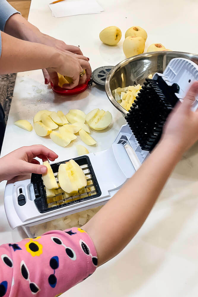 A person peeling and coring apples on a white counter, with a large metal bowl beside them, and multiple peeled apples lined up.