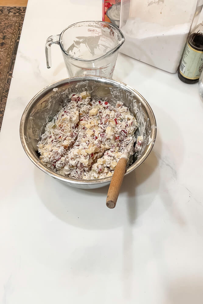 A metal mixing bowl filled with prepared Dixie salad, a creamy pomegranate salad, with a wooden spoon resting inside the bowl.