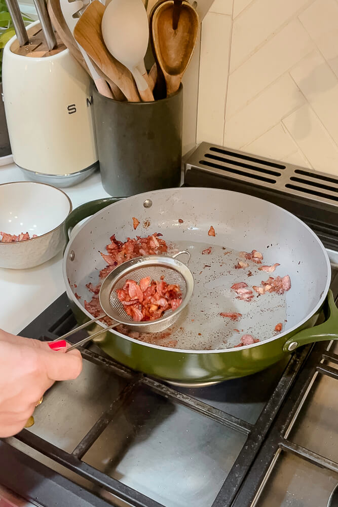 Straining cooked bacon from the skillet with a mesh strainer