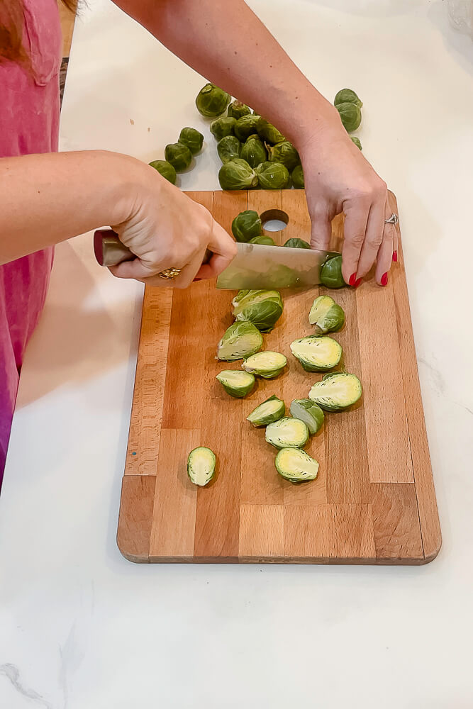 Hands cutting Brussels sprouts in half on a wooden cutting board