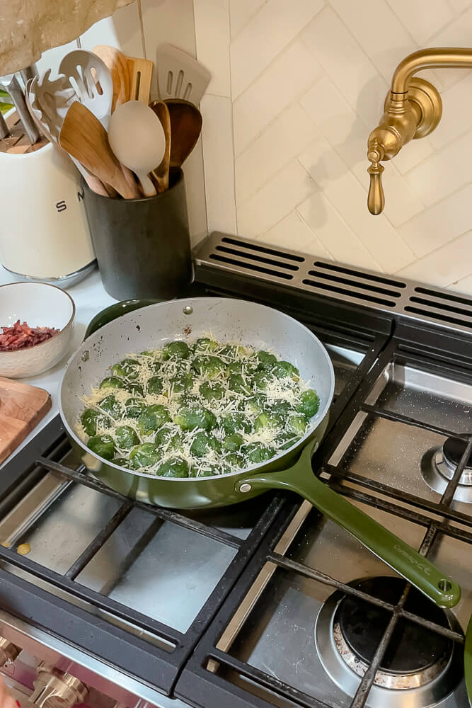 Brussels sprouts cooking in a green skillet with a sprinkle of Parmesan cheese