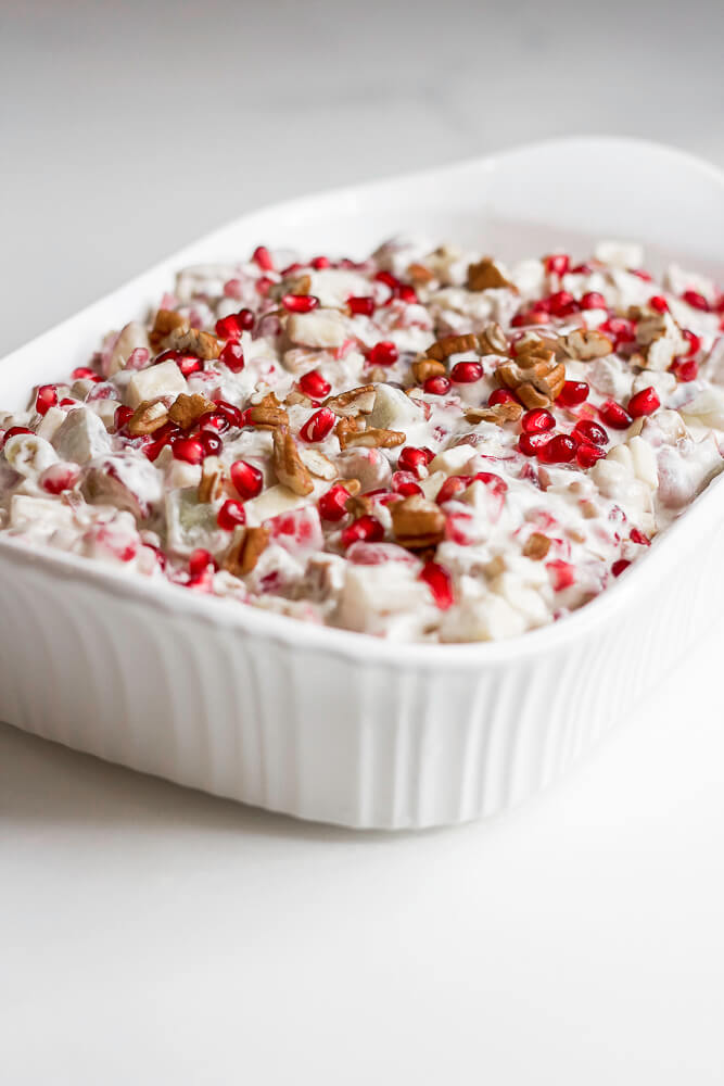 A serving dish filled with Dixie salad, also known as pomegranate salad, topped with red pomegranate seeds and chopped pecans for garnish.