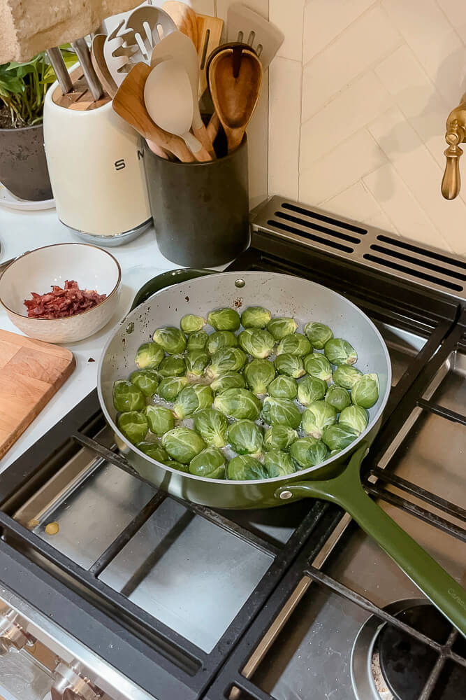 Brussels sprouts boiling in a green skillet on a stovetop