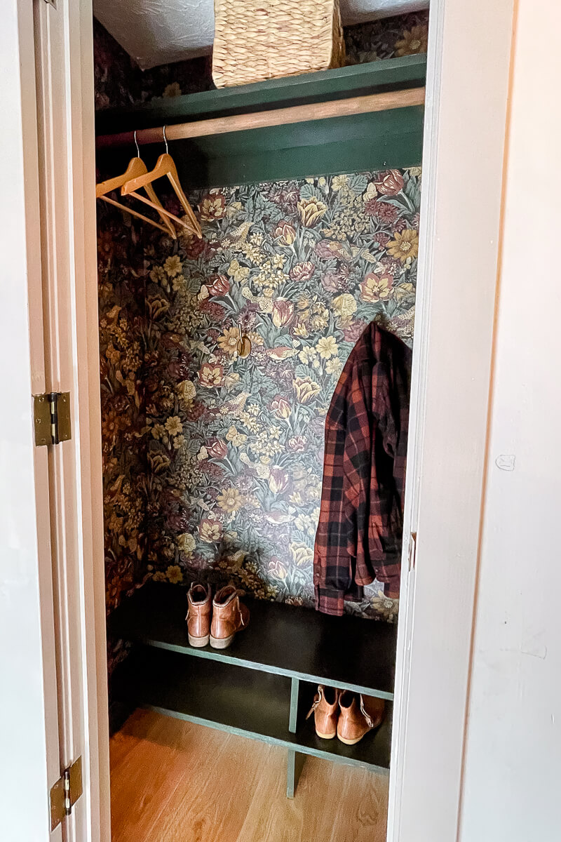 Inside of a beautiful coat closet makeover with designer wallpaper and green shelves and trim