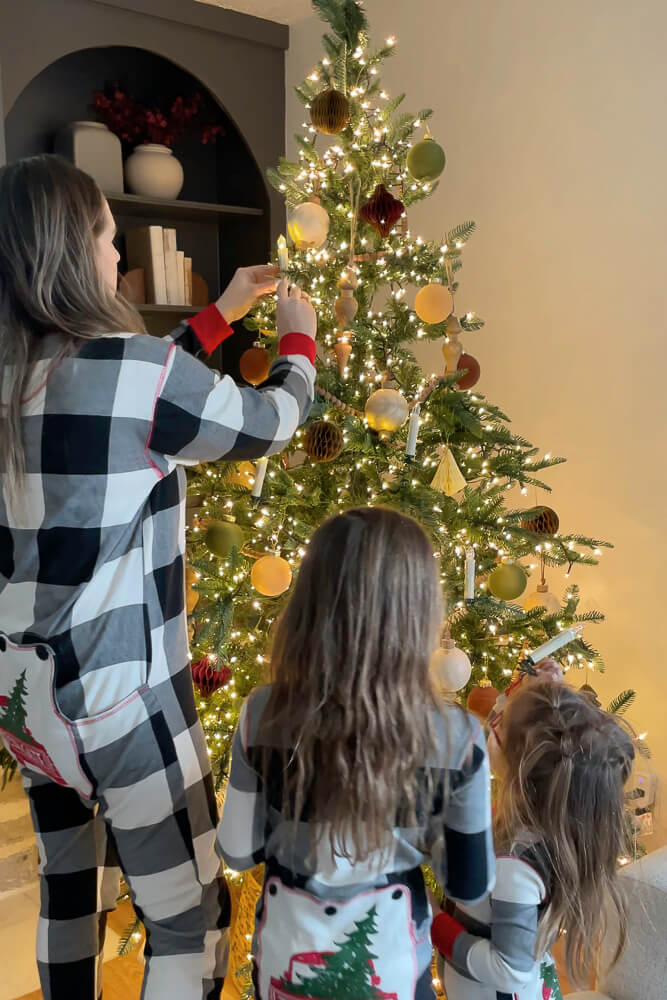 mom and girls decorating a christmas tree in fun pajamas