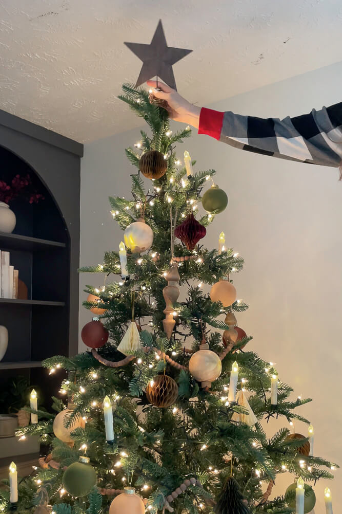 Placing wooden star topper on christmas tree