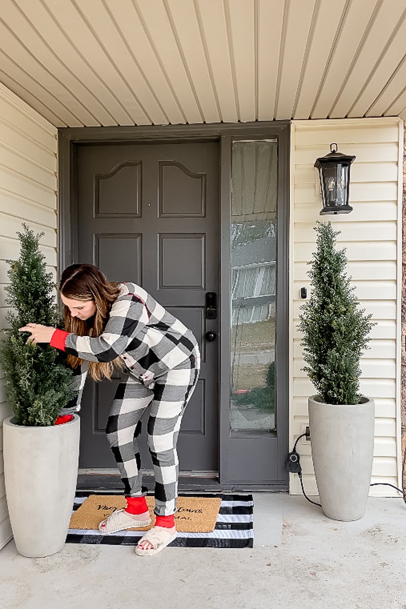 Woman placing faux cedar topiaries in concrete planters on front porch