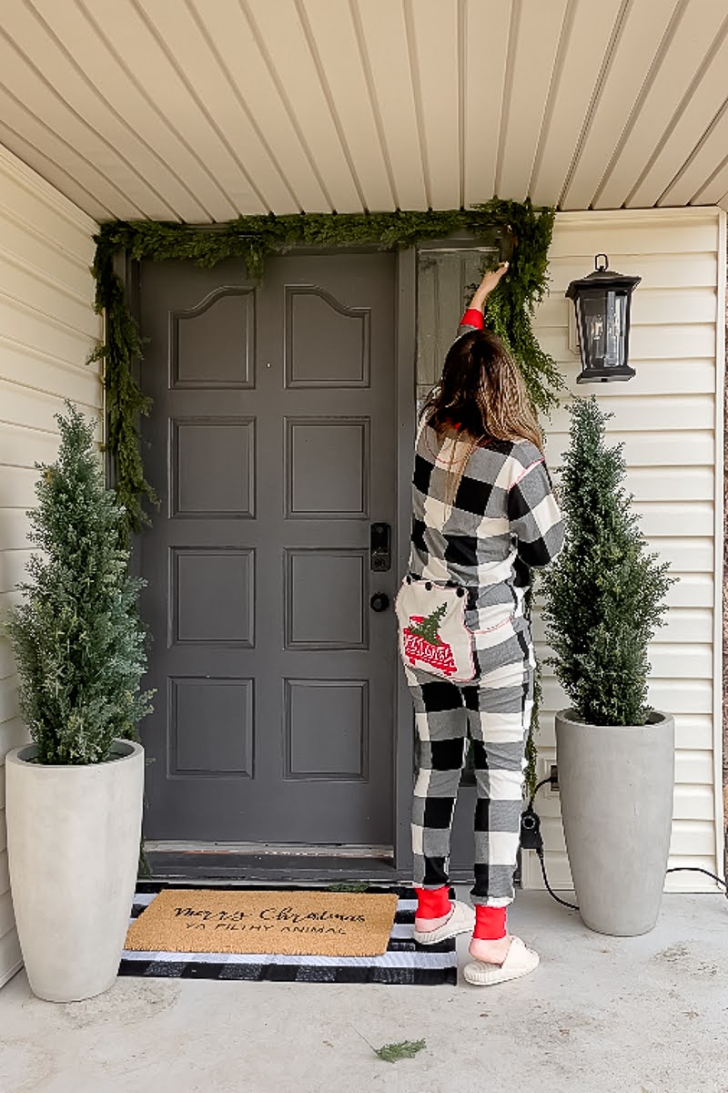 Lading putting up faux Norfolk Pine Garland onto front door of front porch for Christmas