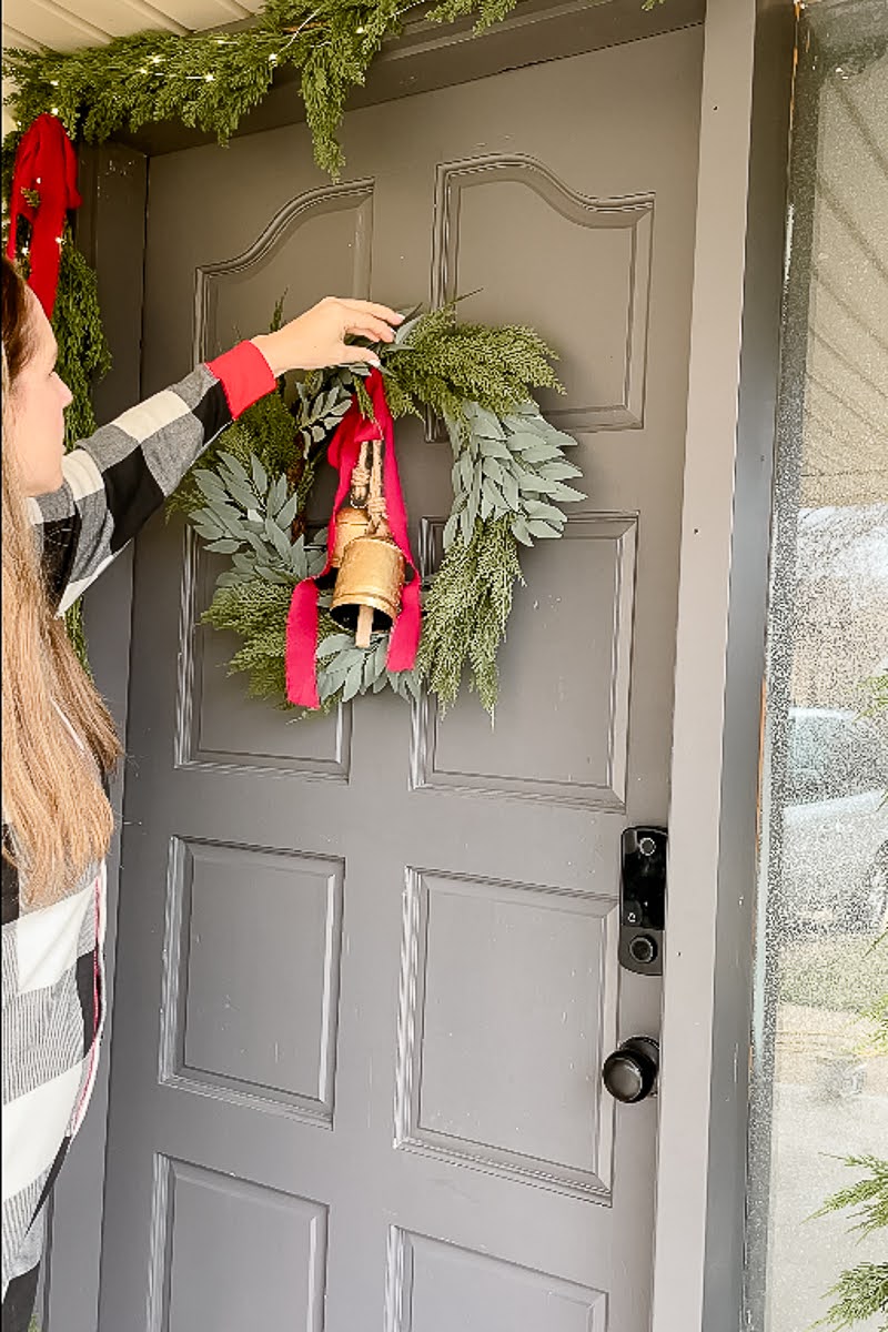 Woman placing bells and bows on Christmas wreath and garland set on front door