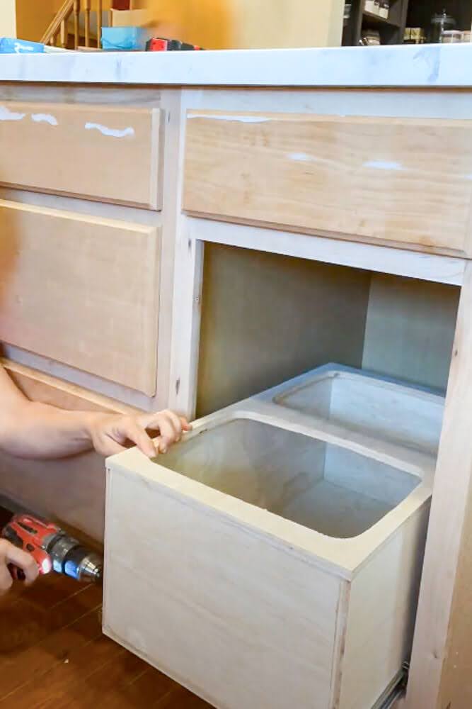 wooden trash drawer getting mounted to drawer slide in cabinet