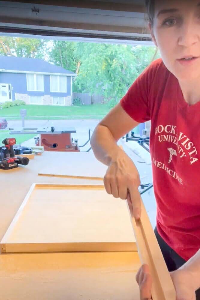 Close-up view of a routed wooden frame piece, showing a precisely cut groove designed to hold the plywood base for a DIY pull-out shelf in a kitchen cabinet