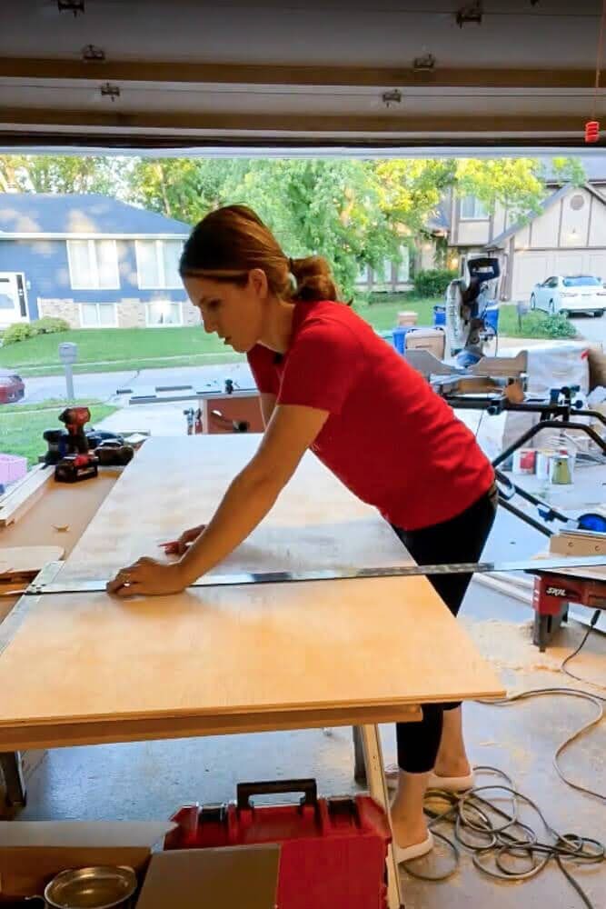 Marking measurements on a piece of plywood with a T-square ruler to ensure accurate cuts for custom pull-out shelves.