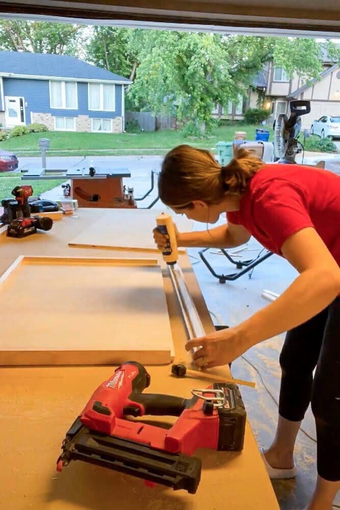 Applying wood glue to the inside groove of a cabinet drawer frame before securing the plywood bottom 