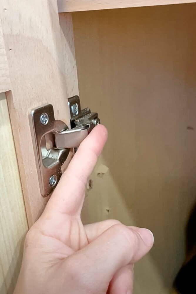 lose-up of a kitchen cabinet hinge protruding into the storage space, highlighting the need for adjustments when installing pull-out shelves.