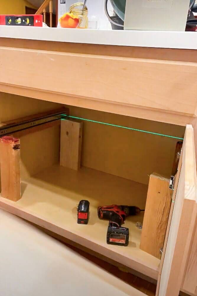 Using a laser level to align and install support blocks inside a kitchen cabinet before mounting 