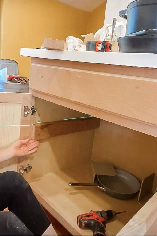 Using a laser level to align a 2x4 bump-out board inside a kitchen cabinet