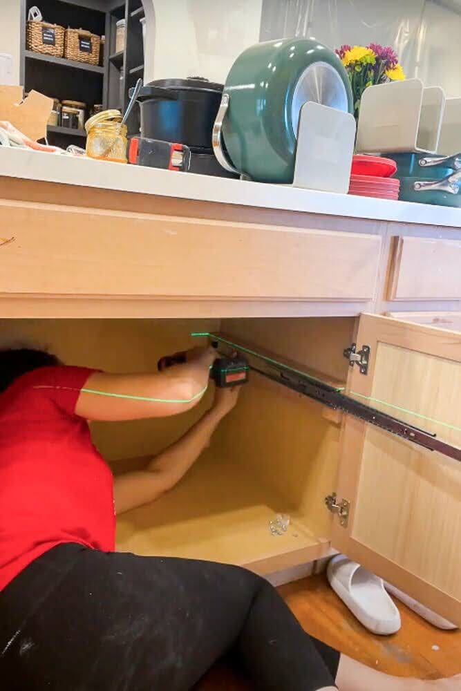 Installing a drawer slide inside a kitchen cabinet for custom pull-out shelves using a drill.