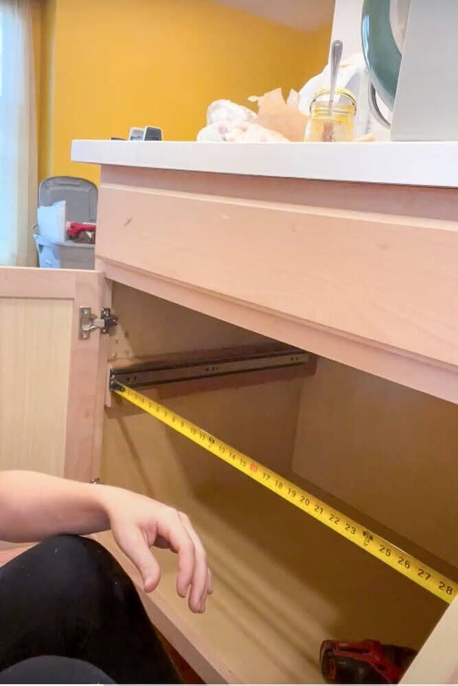 Using a tape measure to check the alignment of drawer slides inside a kitchen cabinet