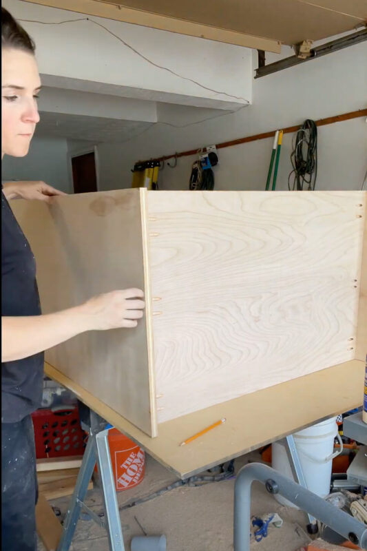 Woman attaching side panel of DIY refrigerator cabinet.