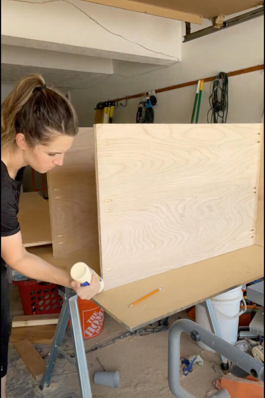 Woman using wood glue while building a kitchen cabinet.