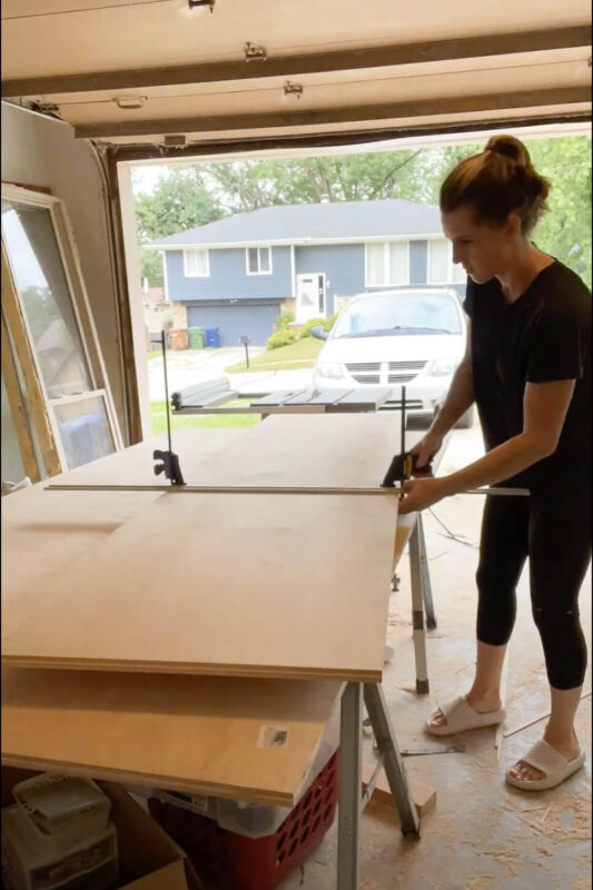 Woman measuring plywood for DIY refrigerator cabinet.