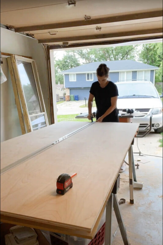 Woman preparing to cut plywood for DIY refrigerator cabinet.