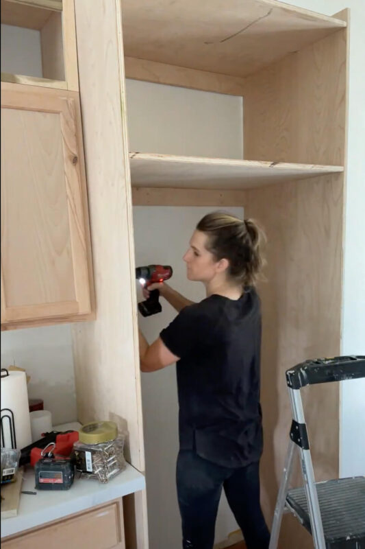 Woman attaching a refrigerator cabinet to other kitchen cabinet.