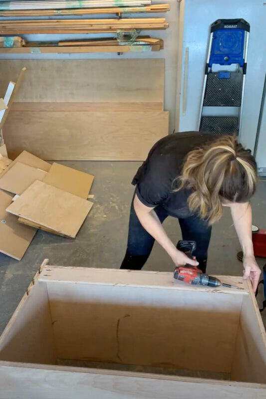 Woman using drill while building refrigerator cabinet.